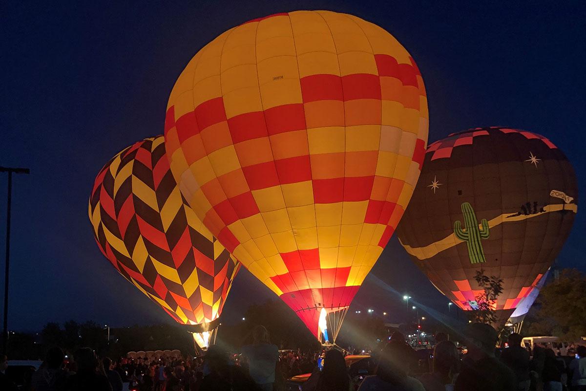 Three large hot air balloons full lit up from the flame at night.